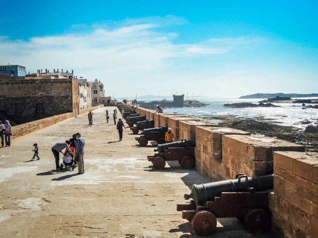 People walking beside historic cannons on Essaouira's seafront ramparts