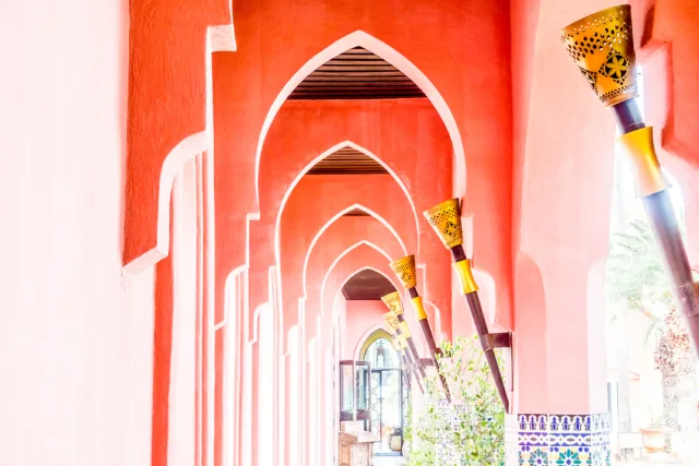 Traditional red archway in the Red City Marrakech with Moorish design and golden lanterns lining the corridor, symbolizing the city’s iconic architectural style.