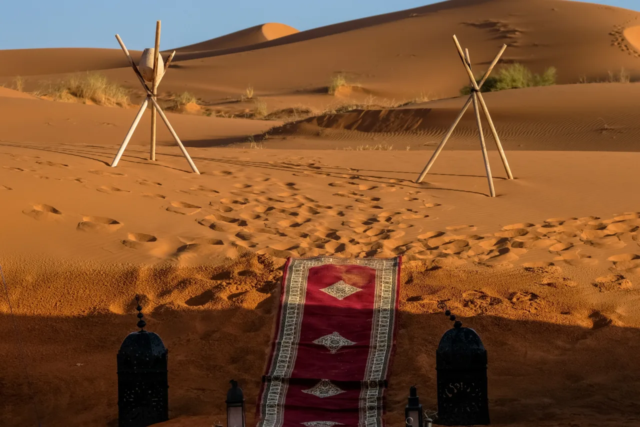 A vertical shot of a red carpet in the middle of lamps and stick tripod with a rock in the distance in the desert