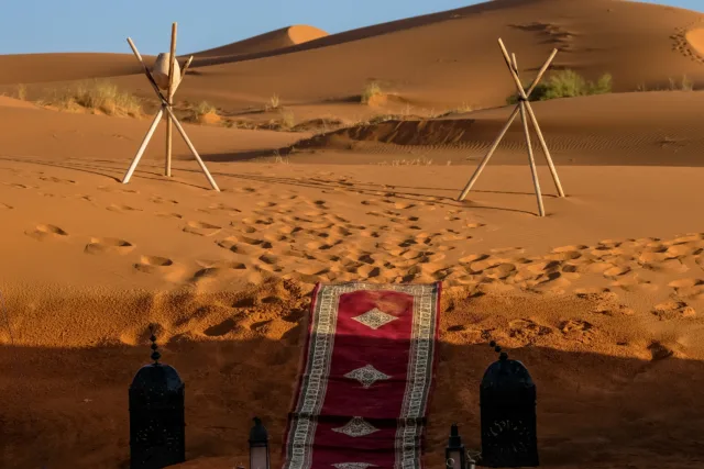 A vertical shot of a red carpet in the middle of lamps and stick tripod with a rock in the distance in the desert