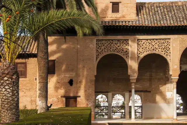 Historic villa with intricate arches and tiled roof surrounded by palm trees and reflecting pool, illustrating the beauty of renovating villas Marrakech.